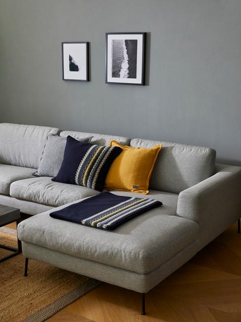 Szary salon w stylu skandynawskim z arożną sofą, poduszkami oraz dekoracjami na ścianie