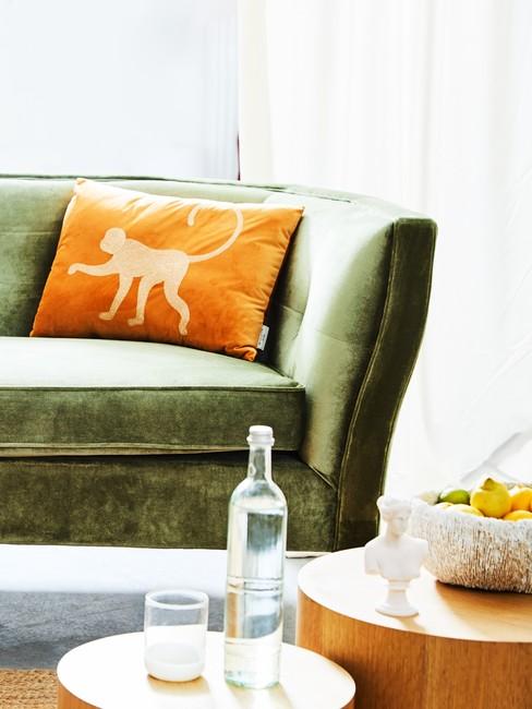 Sofa w kolorze oliwkowym z pomarańczową poduszką oraz drewnianymi stolikami