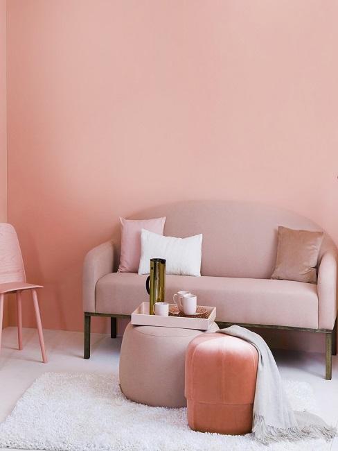 Kleines Wohnzimmer einrichten Ein kleines Sofa in Rosa vor einer Wand in Rosa mit hellem Teppich und einem Pouf mit Tablett anstatt eines Couchtischs