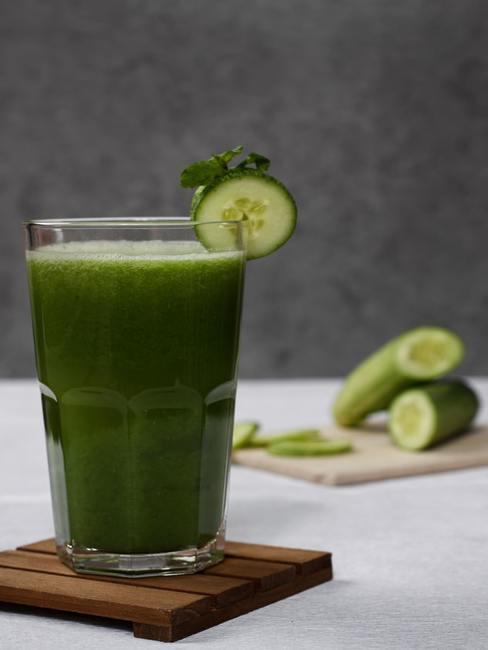 Zielone smoothie w wysokiej szklance na drewnianym podstawce