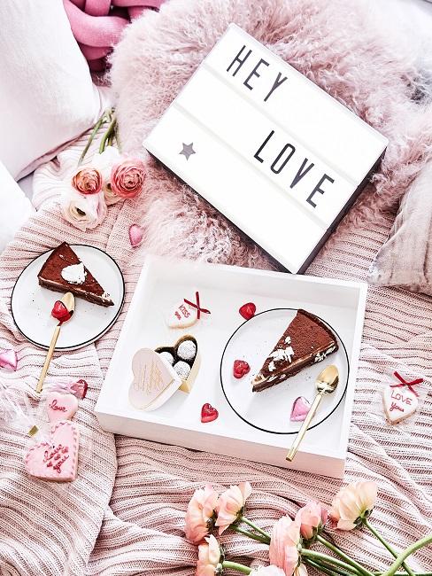 Tablett mit Kuchen auf rosa Bett mit Kissen und Decken