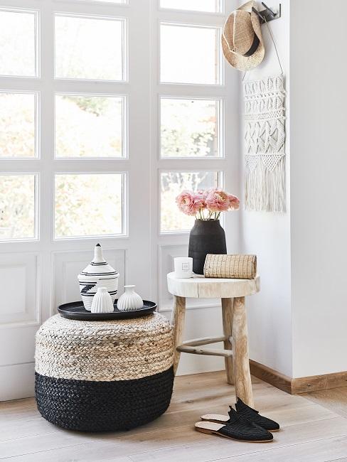 Holzhocker neben Pouf mit Deko vor großer Fensterfront