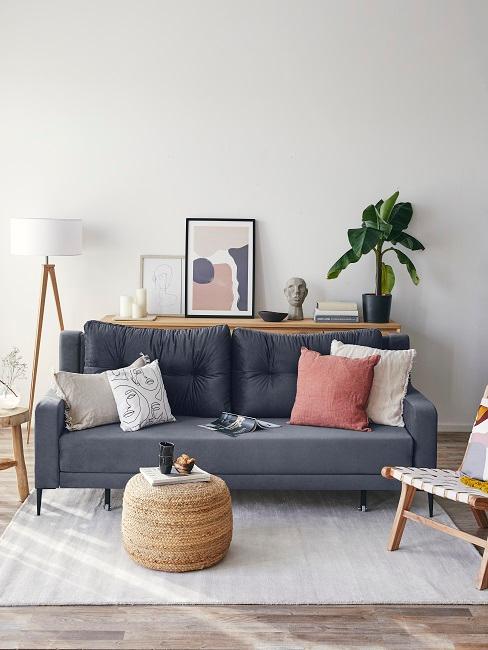 Graues Sofa mit Pouf aus Jute neben Kissendeko, Wandbildern und einer Pflanze