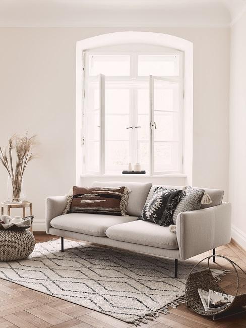 Boho-Wohnzimmer mit beigefarbenen Wänden, Ethno-Kissen auf beigen Sofa und grafischem Teppich