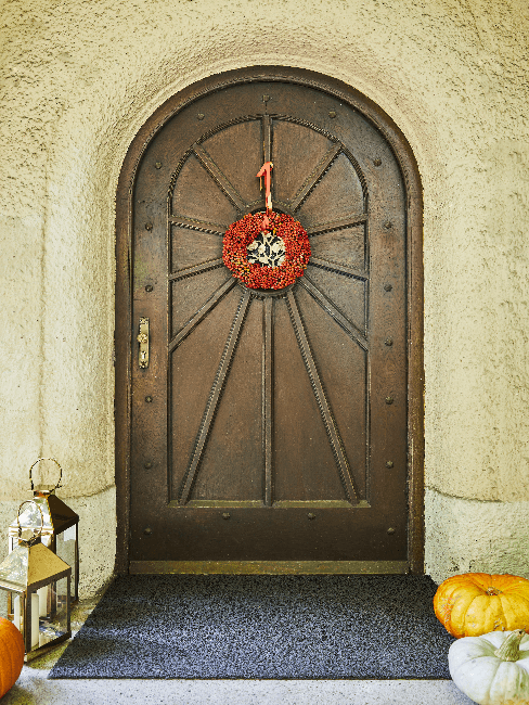 Brown front door with red wreath and lanterns and pumpkins as decoration