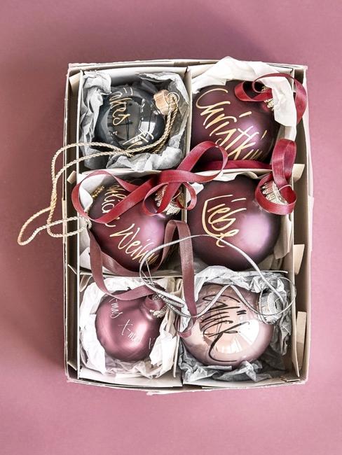 Eingepackte Christbaumkugeln auf rosa Untergrund