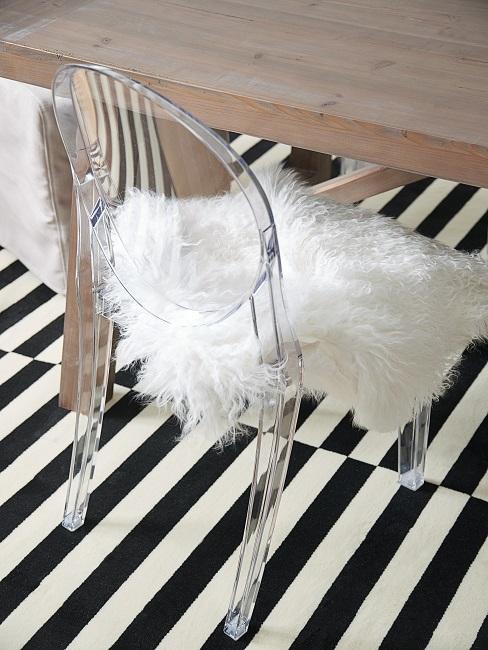 Designklassiker Ghost Chair als Designklassiker mit Lammfellauflage an einem Esstisch, auf einem gestreiften Teppich