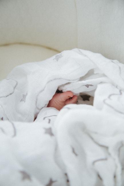 bébé-dans-lit Petit pied de bébé dans draps de lit blancs
