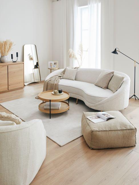 Jasny salon z białą, zaogrągloną sofa, krzesłem, beżowym pufem i okrągłym stolikiem kawowym