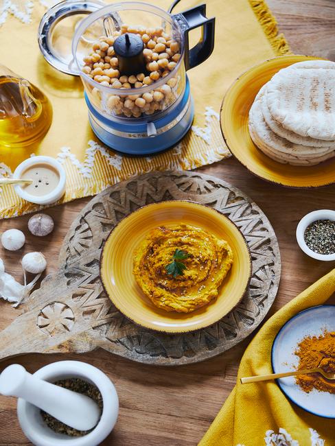Hummus w żółtej miseczce na drewnianej tacy