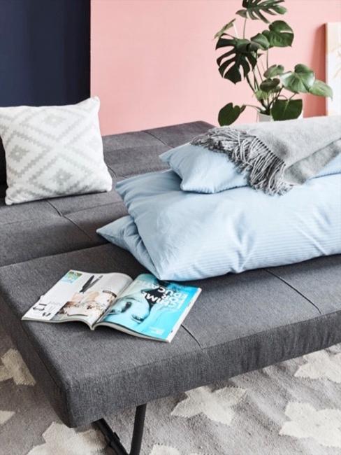 Divano Futon in grigio, ripiegato, su di esso una coperta, un cuscino e una rivista