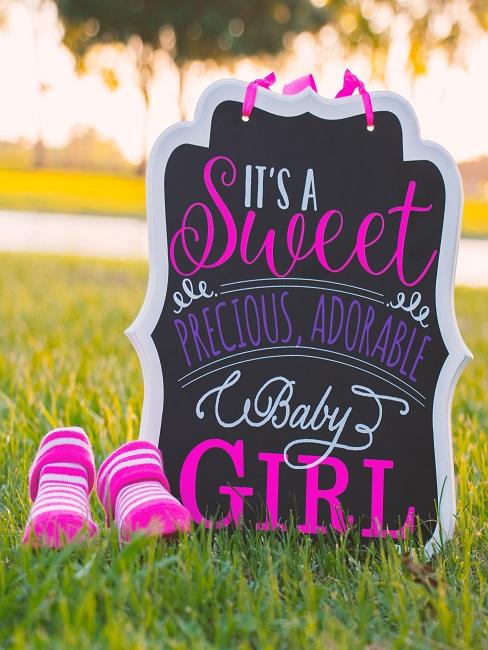 Geschenke zur Geburt Schild "It´s a sweet baby girl" auf einer Wiese neben pinken Schuhen als Geschenk zur Geburt
