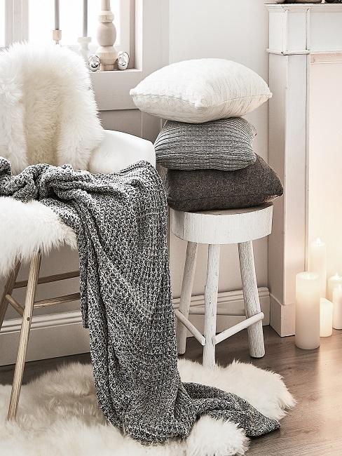 salón escandinavo una silla y un taburete blanco con decoración textil: una piel blanca, una manta gris y unos cojines pequeños