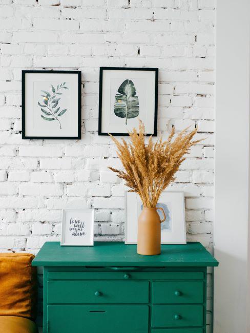 minimalism-banner mur de briques peint en blanc, style rustique, minimaliste, avec une commode verte posee devant ce mur, cadres blancs, vase avec fleurs sechees