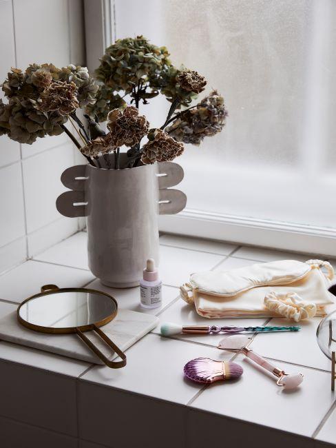 Ranger son maquillage rebord de fenetre avec accessoires de maquillage disperses, miroir et fleurs sechees dans un vase