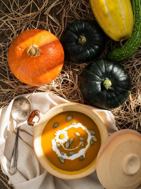 Repas d’Halloween soupe de potiron dans un bol entouree de citrouilles de tailles et couleurs differentes