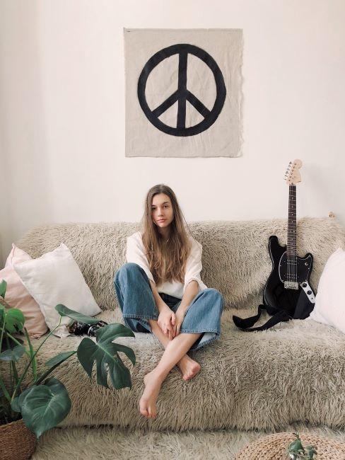 festa hippie ragazza hippie seduta sul divano con simbolo della pace appeso al muro