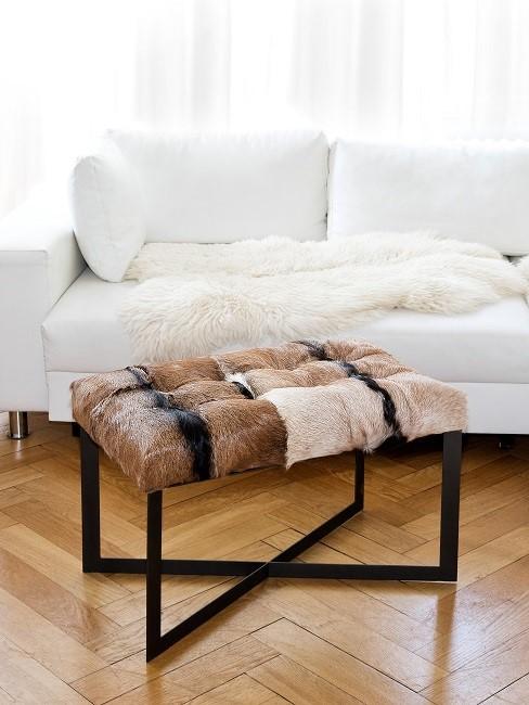 Fellhocker in braun vor weißem Sofa
