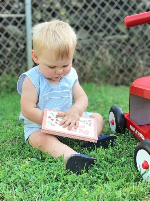 Geschenke zum 1. Geburtstag Baby mit Buch auf Wiese