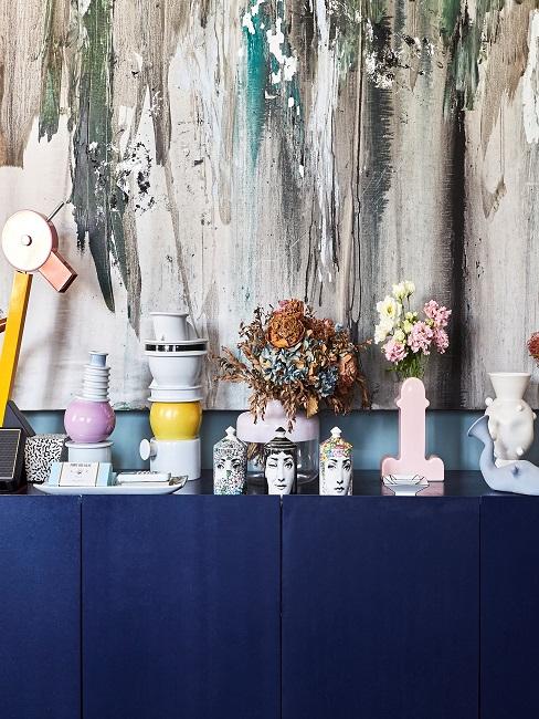 Viel bunte Deko auf blauem Sideboard vor einem Gemälde