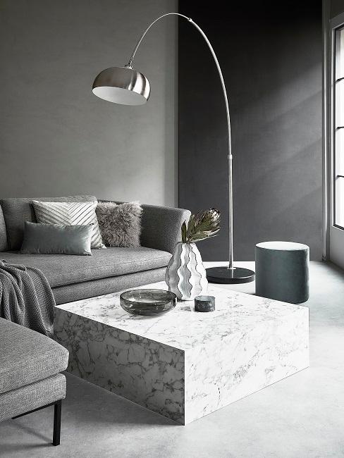 Wohnzimmer mit grauer und schwarzer Wand, grauem Sofa, Mamortisch und silbernen Stehleuchte