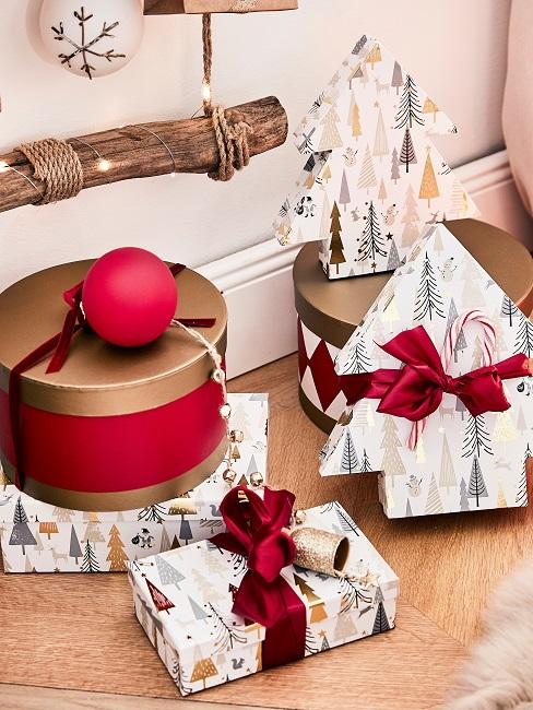 Mehrere verpackte Geschenke in Geschenkpapier und Boxen auf dem Boden vor einer Holzleiter mit Weihnachtskugel und Lichterkette