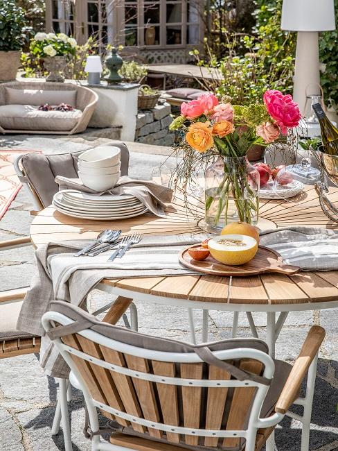 EIne große Terrasse mit rundem Tisch, darauf bunte Sommerblumen als Deko