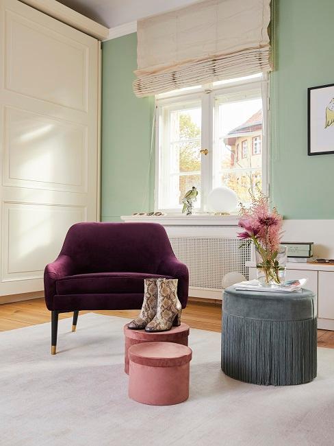 Schlafzimmerecke von Tamara Gräfin von Nayhauß mit einem Sessel in Violett vor Aufbewahrungsboxen in Rosa und einem Pouf in Blaugrau, im Hintergrund eine Wand in hellem Grün