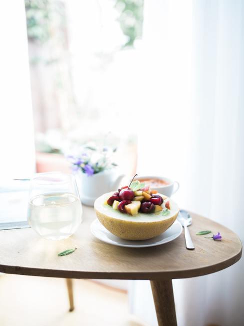 Mesa de madera con un platillo sobre el que hay medio melón con trozos de frutas dentro