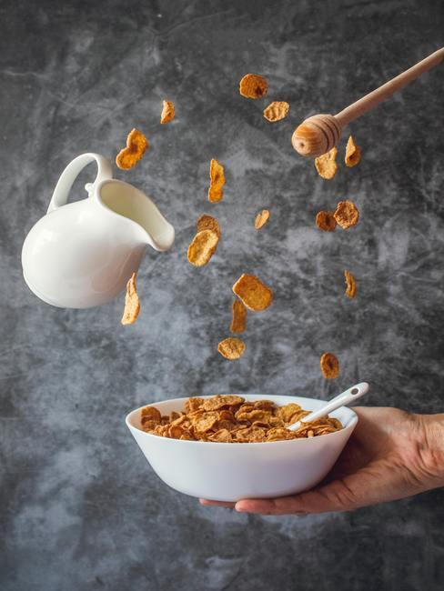 Bol con copos de maiz cayendo, una jarra de leche y miel