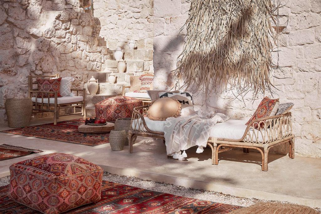 Terraza étnica con decoración oriental, pufs y sillas de madera, con gran muro de piedra