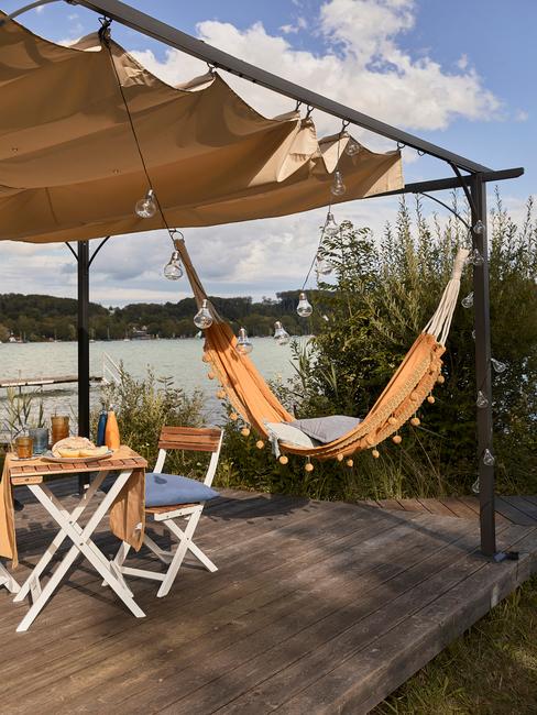 glamping-banner Vacaciones glamping con tarima al borde de un lago, hamaca, mesa y sillas de madera