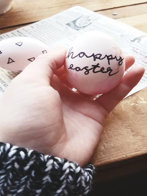 Oeuf tenu dans une main d'enfant avec écrit en noir happy easter
