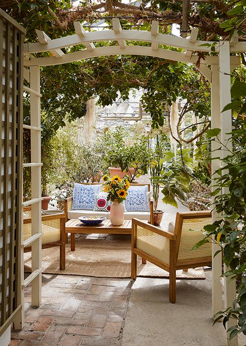 salon de jardin en bois dans une serre avec plantes vertes et vase avec tournesol