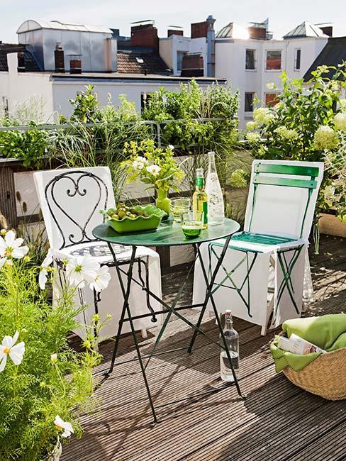 balcon avec sol en bois, chaises et table en métal vert, plantes de balcon
