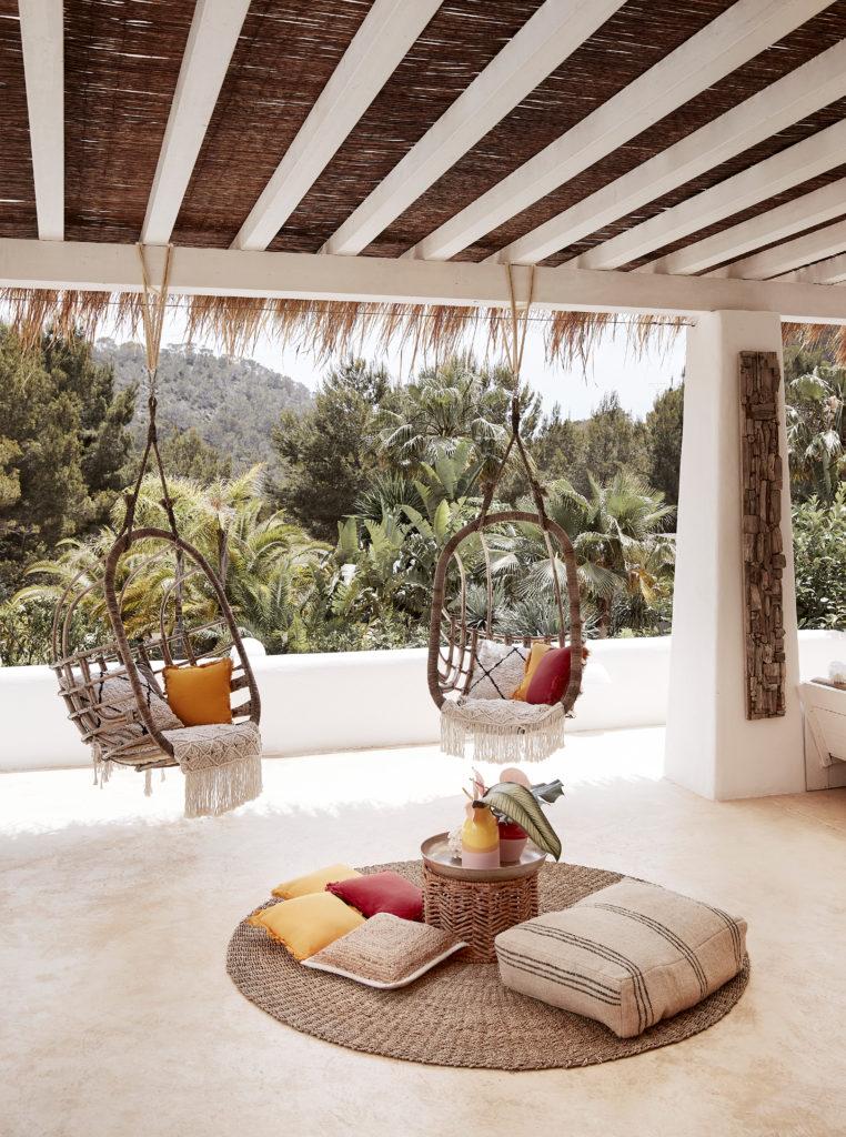 fauteuils suspendus, coussins au sol et tapis en jute sur une terrasse couverte,