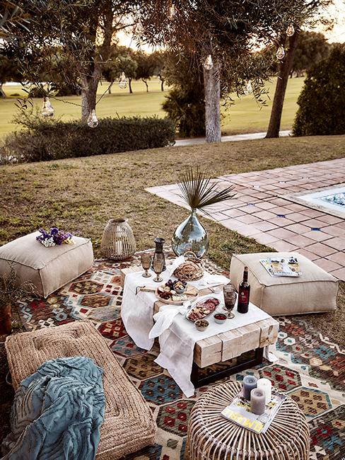 pique nique au fond du jardin avec grand tapis vintage, poufs et coussins, guirlandes lumineuses dans un arbre