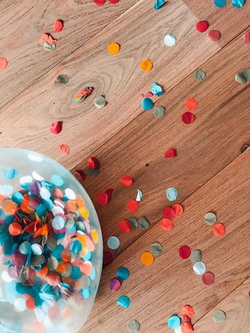 Confettis de toutes les couleurs éparpillés sur une table en bois et à l'intérieur d'un bocal en verre