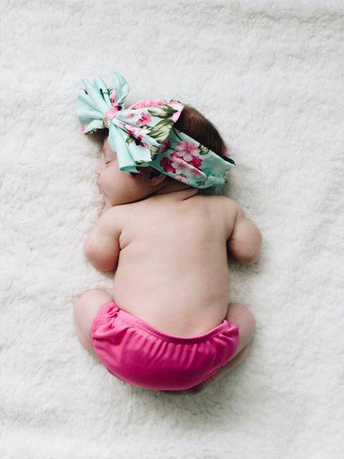 matelas-bébé nouveau-ne en couche-culotte rose et un grand nœud sur la tete dort paisiblement allongé sur une matiere blanche duveteuse