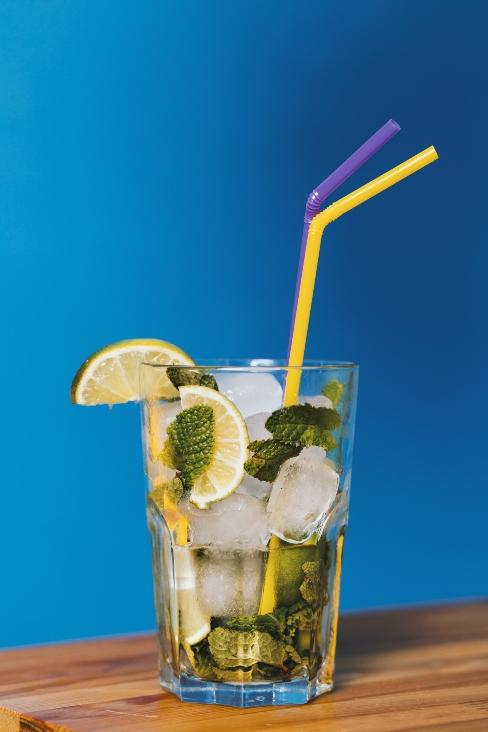 cocktail avec citron et glaçon, avec deux pailles colorées sur fond bleu