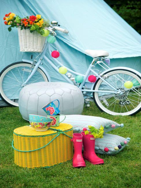 Jardin avec vélo bleu, guirlande multicolore, coussins à pompons et table basse en osier jaune