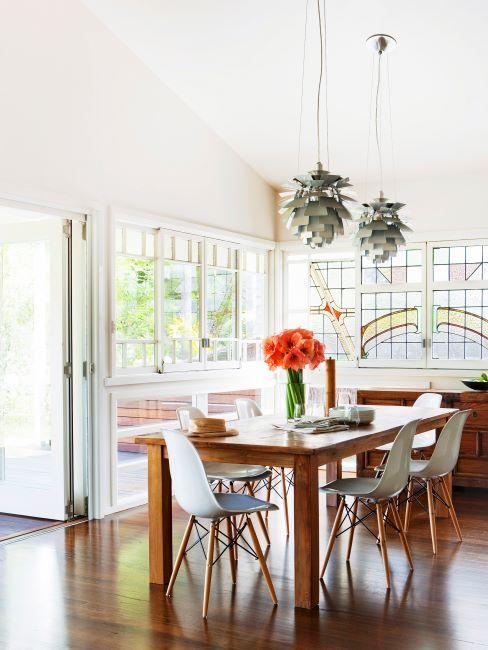 Salle à manger aux murs crème, à plafond haut, suspensions originales, vitres en verre teinté, table et chaises en bois