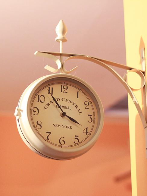 horloge gare en métal accroché à un mur jaune pastel