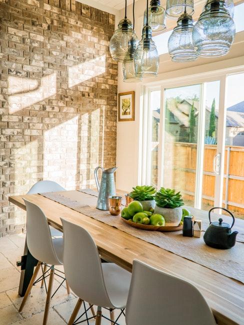 Salle à manger avec table en bois massif, chaises en plastique, suspensions en verre et mur en brique