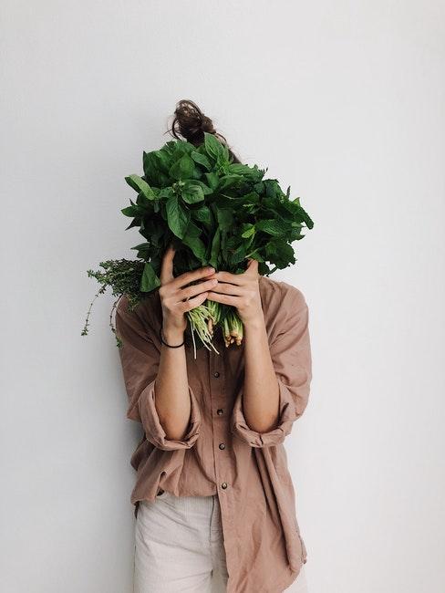 femme vêtue de beige et crème tenant des légumes devant son visages