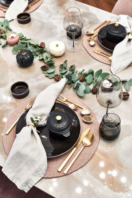 table de noel avec serviettes blanc creme, assiettes noir, couverts dores et decoration florale