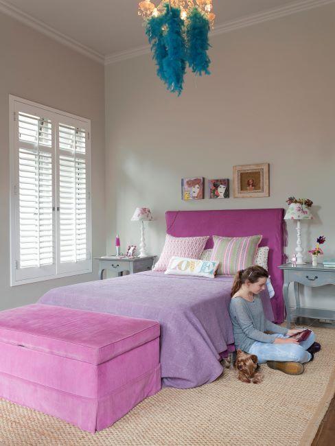 une fille adolescente assise par terre a regarder son tablett dans sa chambre claire avec lit rose vif