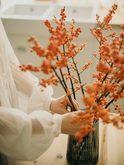 femme décorant son intérieur avec des fleurs d'automne oranges dans un vase en verre foncé