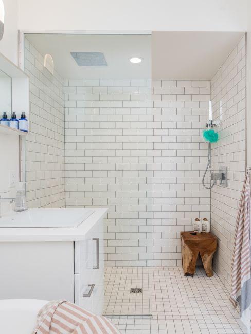 salle de bains à carreaux crème, meuble blanc, douche et tabouret en bois