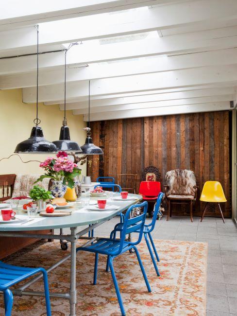salle à manger avec murs en bois, suspensions industrielles, tapis oriental vintage et chaises bleues